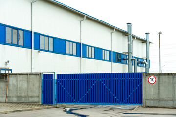 The facade of an industrial building or warehouse with large windows. Modern factory buildings or warehouses. Large metal gates and a concrete fence.
