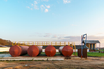Large metal tanks for storing gasoline, gas or oil. Red barrels on the territory of the enterprise under the open sky during sunset.