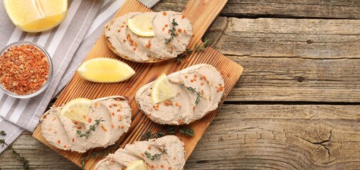 Tasty bruschettas with pate, lemon slices, thyme and dried carrot flakes on wooden table, flat lay. Space for text