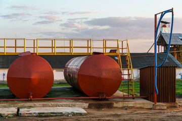 Large metal tanks for storing gasoline, gas or oil. Red barrels on the territory of the enterprise under the open sky during sunset.