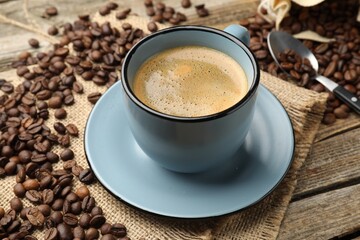 Obraz premium Aromatic coffee in cup and beans on wooden table, closeup
