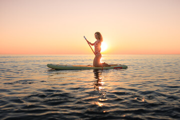 Young woman walking on stand up paddle sup boards by the sea during summer vacation