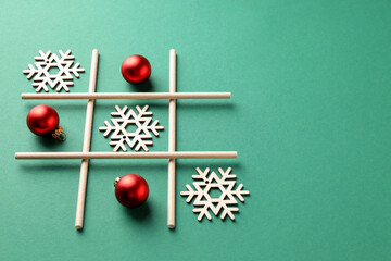 Tic tac toe game made with baubles and wooden snowflakes on green background. Space for text