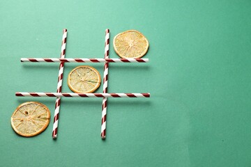Tic tac toe game made with dry orange slices on green background. Space for text