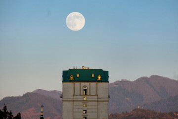 Large, bright full moon setting over a building and mountains