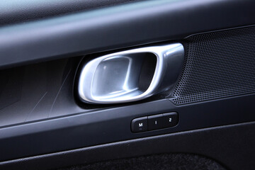 Car door handle. Close-up of a modern car's interior door handle in brushed metal. Features a black panel with seat memory settings buttons and a speaker grille, creating a premium and functional desi