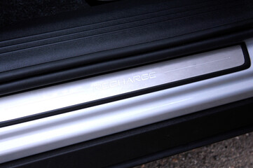 Close-up of a brushed aluminum door sill plate from a modern electric car. It features the 'RECHARGE' branding, highlighting its eco-friendly technology, set against black textured plastic.