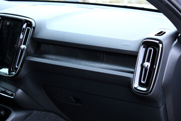 Close-up of a modern car's dashboard from the passenger side. Features a black textured design with a vertical air vent, chrome trim, a patterned insert, and an airbag safety system. Car air bag.