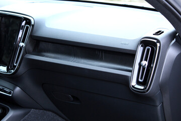A view of the dashboard of a modern car from the passenger side. It features black textured design, stylish vertical air vents with chrome trim, a patterned insert, and airbag. Car glove compartment.