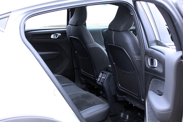 View of the spacious rear cabin of a modern car. It features black combined leather and Alcantara seats with white stitching, seatback storage pockets, and an open rear door. Close up rear seats.