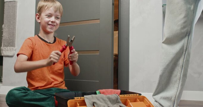Boy plays with pliers repeatedly opening and closing jaws while observing movement. Father places screwdriver back into toolbox maintaining safe workspace