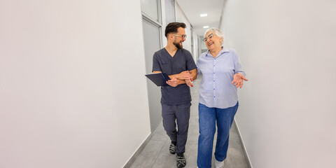 Male doctor and elderly patient laughing and talking while walking arm in arm through hospital lobby