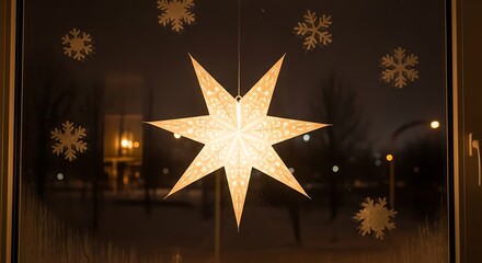 Illuminated eight-pointed paper star decoration hangs in a window alongside festive snowflake decals during wintertime.