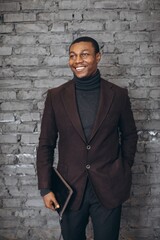 Smiling young businessman holding tablet standing against brick wall