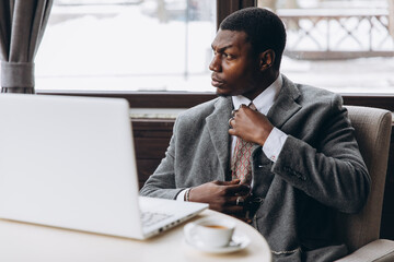 Thoughtful businessman adjusting tie while working on laptop