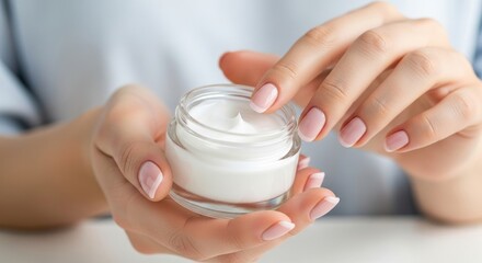 Woman gently touching rich white face cream inside a glass jar