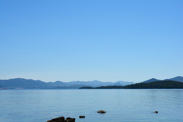 A wide panoramic view of the modern Peljesac Bridge stretching across the sea as seen from the peaceful coastal village of Drace on the peninsula