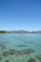 Obraz premium A vertical shot of the transparent turquoise Adriatic Sea in Sreser on the Peljesac peninsula with the mountains of mainland Croatia visible on the horizon under a blue sky