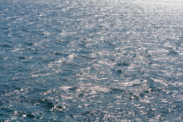 Sunlight creates a bright glittering pattern of reflections on the rippling surface of deep blue sea water during a sunny day.