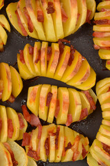 A close up vertical shot of golden roasted hasselback potatoes stuffed with small pieces of crispy bacon on a dark surface