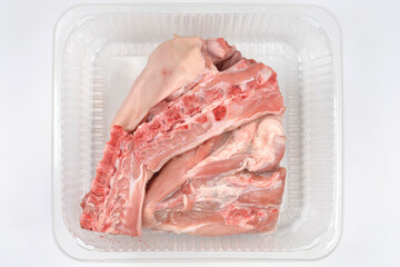 A top view shows fresh raw suckling pig meat with skin and bones placed inside a transparent plastic container on a white background.