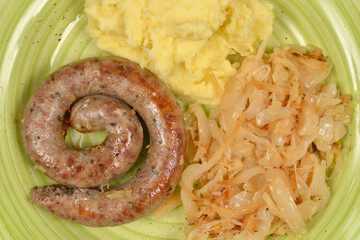A detailed top view of a grilled spiral sausage served with creamy mashed potatoes and braised sauerkraut on a green plate