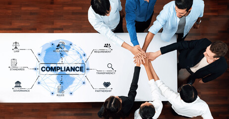 A diverse team collaborates over a table with hands joined, focusing on compliance strategies, represented by symbols of law and regulation. Trope