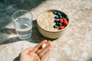 Close-up of hand holding a supplement pill with healthy breakfast in the background &ndash; concept of wellness and daily routine
