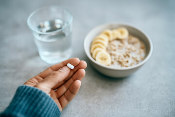 Close-up of hand holding a supplement pill with healthy breakfast in the background &ndash; concept of wellness and daily routine
