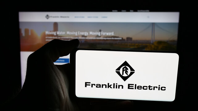 Stuttgart, Germany - 12-18-2025: Person holding mobile phone with logo of US company Franklin Electric Co. Inc. on screen in front of web page. Focus on phone display.