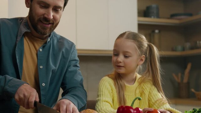 Happy family at kitchen Caucasian father talking with little child girl daughter kid communicate friendly talk smiling cut bread cutting slicing baguette coocking food breakfast dinner lunch at home