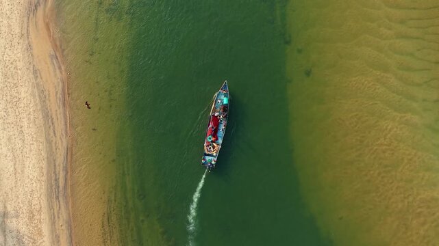 Fishing boat with red nets and crew navigating through deep green sea, creating foamy water trails captured from aerial view, symbolizing teamwork, labor, and traditional livelihood at sea
