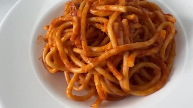 Bucatini pasta Amatriciana, Italian pasta with tomato sauce, pecorino cheese, and guanciale bacon in a white dish, tracking shot