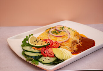Imagen horizontal de un plato de lasag&ntilde;a con ensalada fresca en fondo color rosa