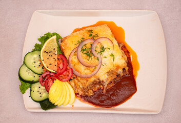 Plano cenital de una porcion de lasa&ntilde;a con ensalada en un plato blanco 