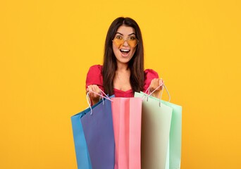 Happy customer. Overjoyed armenian woman in sunglasses holding bright shopping bags, posing and...