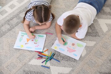 Children drawing with crayons on floor at home, above view