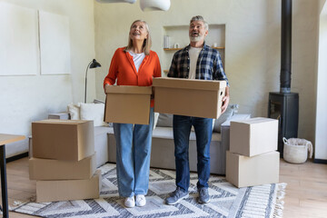 Senior couple standing in living room with cardboard boxes on moving day