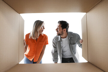 Excited couple looking into cardboard box on white background, view from inside package