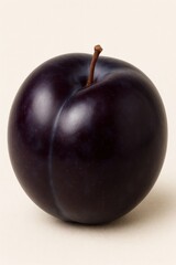 A dark plum sits on a neutral surface, showcasing its deep color and shape.