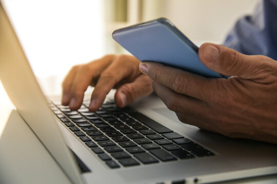 Closeup man hands using smartphone and laptop. Businessman works with computer and mobile phone - Powered by Adobe