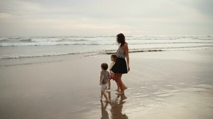 Mother walking with her son and daughter along the beach at sunset, enjoying family time. Summer vacation, and outdoor lifestyle