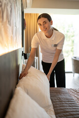Young woman in hotel uniform doing bed in a hotel room