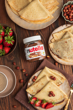 Lviv, Ukraine - June 19, 2025: Crepes with Nutella and strawberries, served with coffee and hazelnuts on a wooden table. Top view