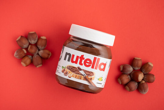 Lviv, Ukraine - June 19, 2025: Nutella jar with hazelnuts on a red background. Top view