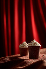 Cozy Hot Chocolate Cups with Whipped Cream and Tweed Texture on Cinematic Red Curtain Background