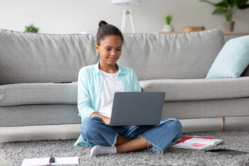 Concentrated teen afro american female student studying at home with laptop, preparing for test, exam, doing homework or watch online lesson. Remote education, device for learning at self isolation