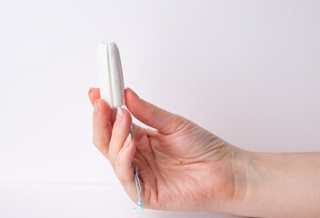 Hand holds a white tampon with blue string against a plain background