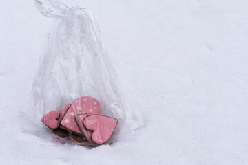 Heart shaped gingerbread cookies with pink icing in a transparent bag lying on snow