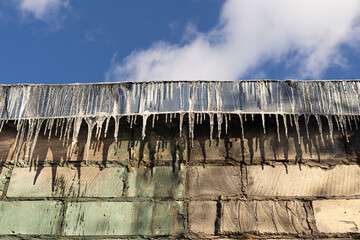 Icicles hanging from the roof edge of a residential house in winter weather